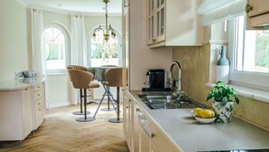 Una cocina moderna con piso de madera, un comedor con dos sillas, una araña y una ventana con una planta en la encimera.