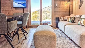 A cozy room with a sofa, chairs, a table, a TV, and a large window with a view of a snowy landscape. - Cosy apartment for 4 guests with WIFI, TV and terrace (Basse-nendaz)