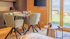 A modern dining area with a table set for four, a television mounted on the wall, and a view of a mountainous landscape through large windows. - Cosy apartment for 4 guests with WIFI, TV and terrace (Basse-nendaz)