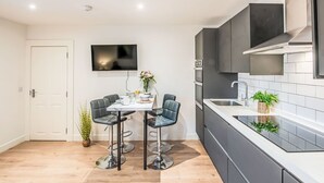 A modern kitchen with a dining area, featuring a TV, dark cabinetry, and a tiled backsplash. - Beautiful apartment for 4 people with WIFI and TV (Nairn)