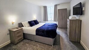 A bedroom with a bed, bedside tables, a wardrobe, a TV, and a window with curtains. - Beautiful apartment for 4 people with WIFI and TV (Nairn)