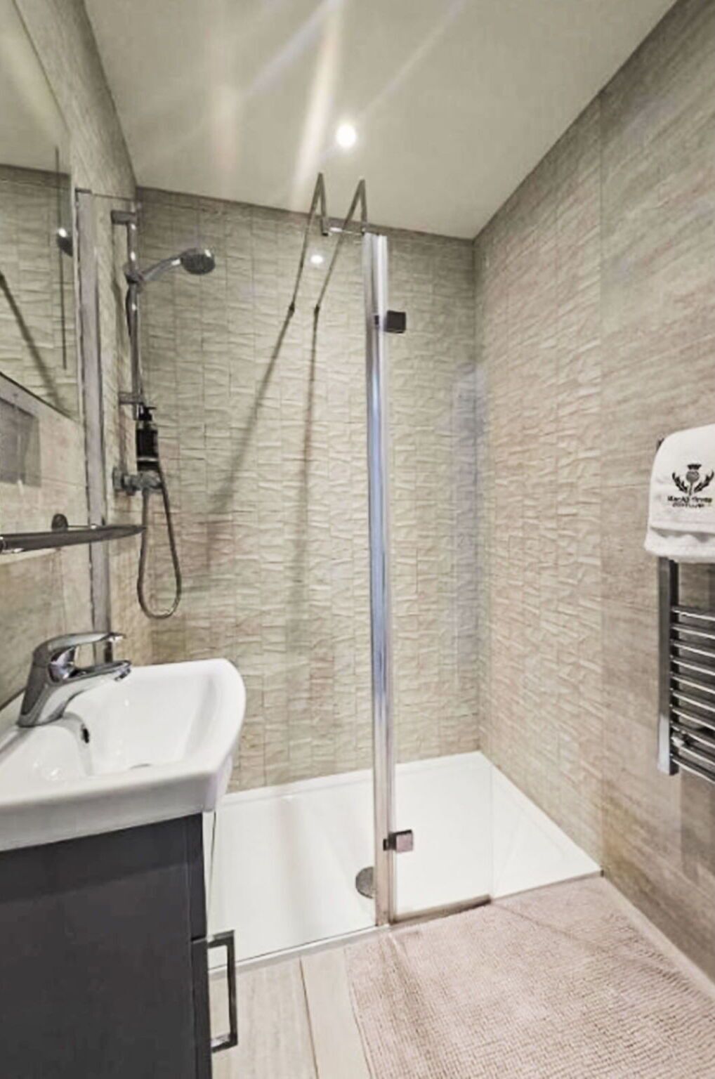 Un baño moderno con cabina de ducha de vidrio, un lavamanos y un perchero para toallas.
