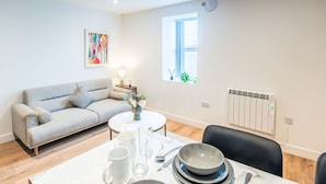 Una sala moderna con un sofá, una mesa de comedor con platos y vasos, una mesa baja con un florero y un radiador en la pared.