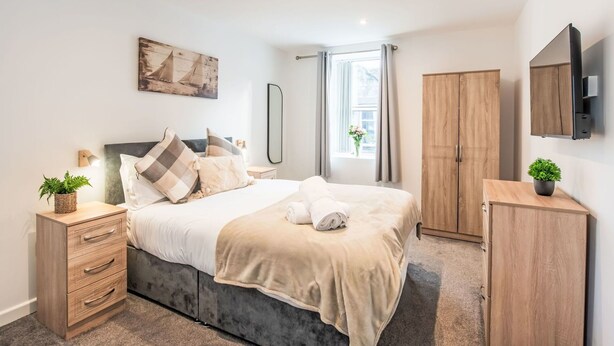 Un dormitorio moderno con cama, mesitas de noche, armario, televisión y ventana con cortinas.