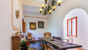 A dining area with a wooden table and chairs, a chandelier, and a view of the street through an arched window. - Beautiful apartment for 7 people with WIFI and patio (Volterra)