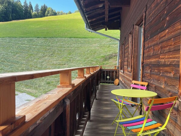 Una terraza de madera con barandilla, una mesa y sillas coloridas, con vista a un campo de césped.