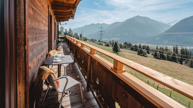 Un balcón de madera con una mesa y sillas, con vistas a un paisaje montañoso.