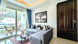 A living room with a sofa, a glass coffee table, a painting on the wall, and a view of the outside.