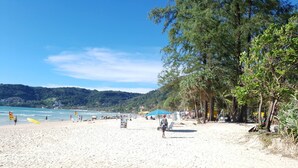 Una playa arenosa con cielo despejado, palmeras y algunas personas.