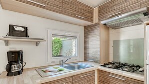 A modern kitchen with a gas stove, a coffee maker, a window, and wooden cabinetry. - Mobile home 35m² with terrace for 8 people, disabled access (Bormes-les-Mimosas)