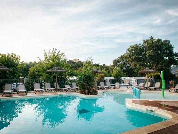 Piscina con sillas de descanso y sombrillas, rodeada de follaje y árboles.