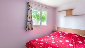 Een slaapkamer met een bed, een raam met gordijnen en een houten plank.