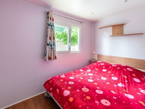 A bedroom with a bed, a window with curtains, and a wooden shelf. - Mobile home with terrace in Bormes-les-Mimosas (Bormes-les-Mimosas)