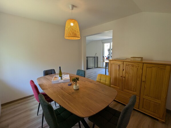 A dining area with a wooden table, chairs, a hanging light fixture, and a cabinet.