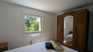 A bedroom with a large bed, a wooden wardrobe, a window with a view of trees, and a radiator. - House for 4 in Gérardmer between lake and mountains with terrace (Gérardmer)