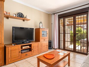 A living room with a TV, wooden cabinets, a small table, and a sliding glass door to a balcony.