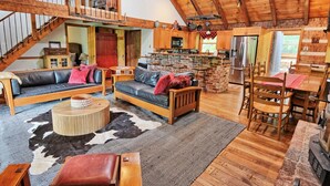 A spacious living area with a wooden staircase, leather sofas, a dining table with chairs, and a kitchen area with a brick island.