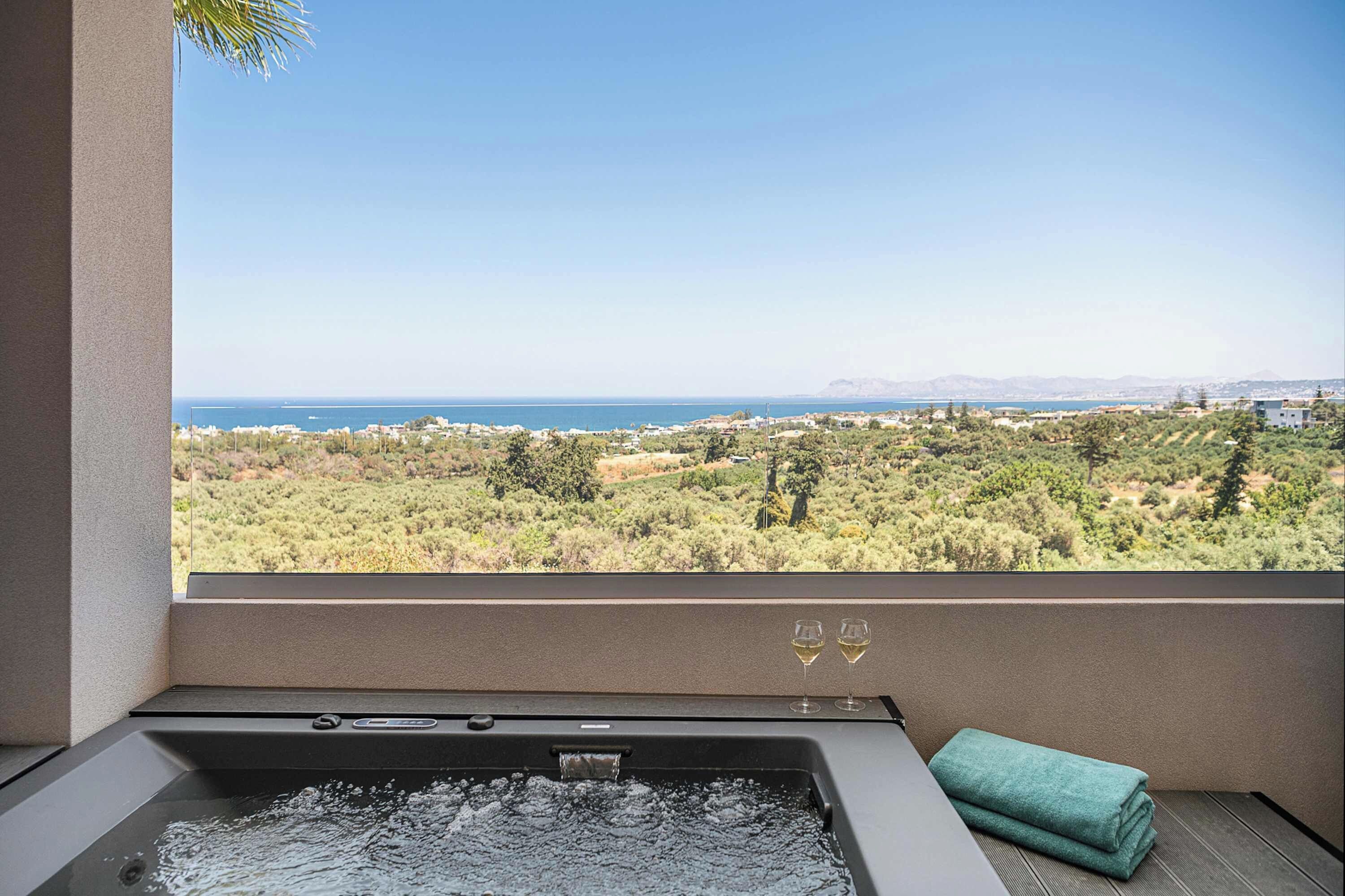 A spa area with a hot tub, a view of the sea, and a window with two wine glasses.