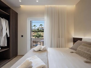 A hotel room with a bed, a seating area with a table and chairs, a wardrobe, and a view of the outdoors. - Kymélia Upper Suite With Private Hot Tub & SeaView (Galatas)