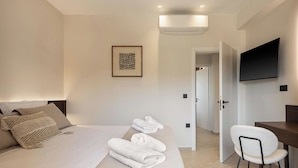 Een moderne hotelkamer met een opgemaakt bed, een bureau met een stoel, een flatscreen televisie en een airconditioning.