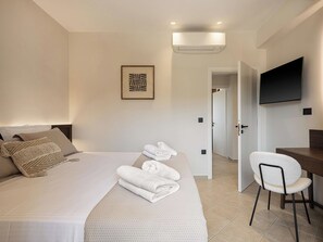 Habitación de hotel moderna con una cama bien hecha, un escritorio con silla, un televisor de pantalla plana y un equipo de aire acondicionado.