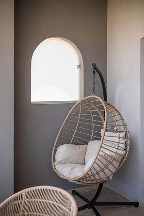 Una silla colgante de mimbre con cojín, ubicada cerca de una ventana de arco.