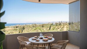 A balcony with wicker chairs, a round table, and a view of a coastal landscape. - Kymélia Upper Suite With Private Hot Tub & SeaView (Galatas)