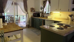 Eine Küche mit Herd, Mikrowelle und Spüle. Ein Holztisch und ein Stuhl befinden sich vor der Tür.