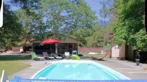 Ein Swimmingpool mit blauer Abdeckung, einer überdachten Sitzgelegenheit und einem roten Sonnenschirm.