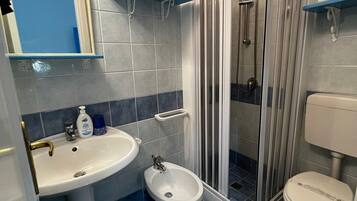 Une salle de bain équipée d’un lavabo sur colonne, d’un bidet, de toilettes et d’une douche à parois de verre.
