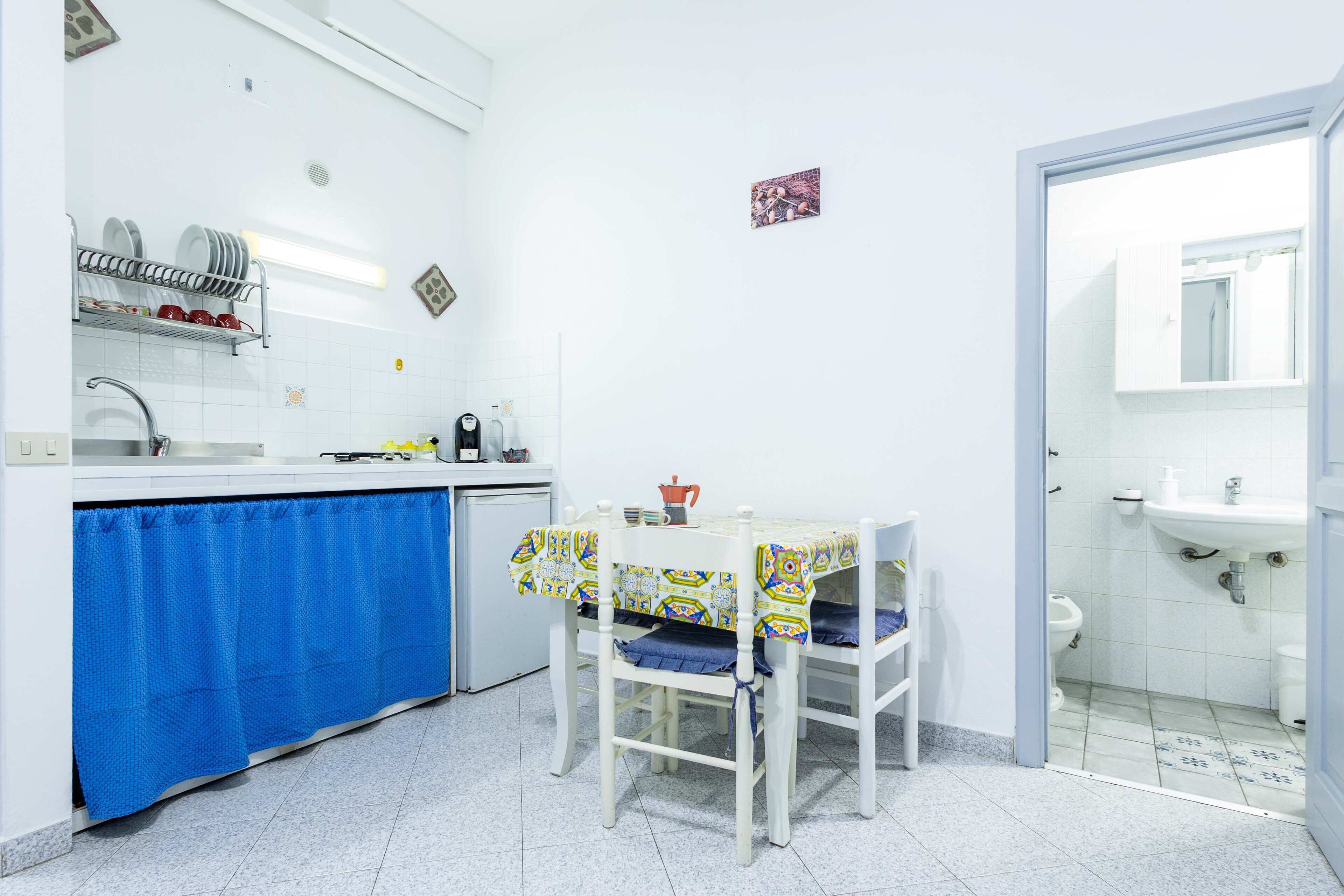 A compact kitchen with a blue curtain, a table with a patterned tablecloth, and a white sink.