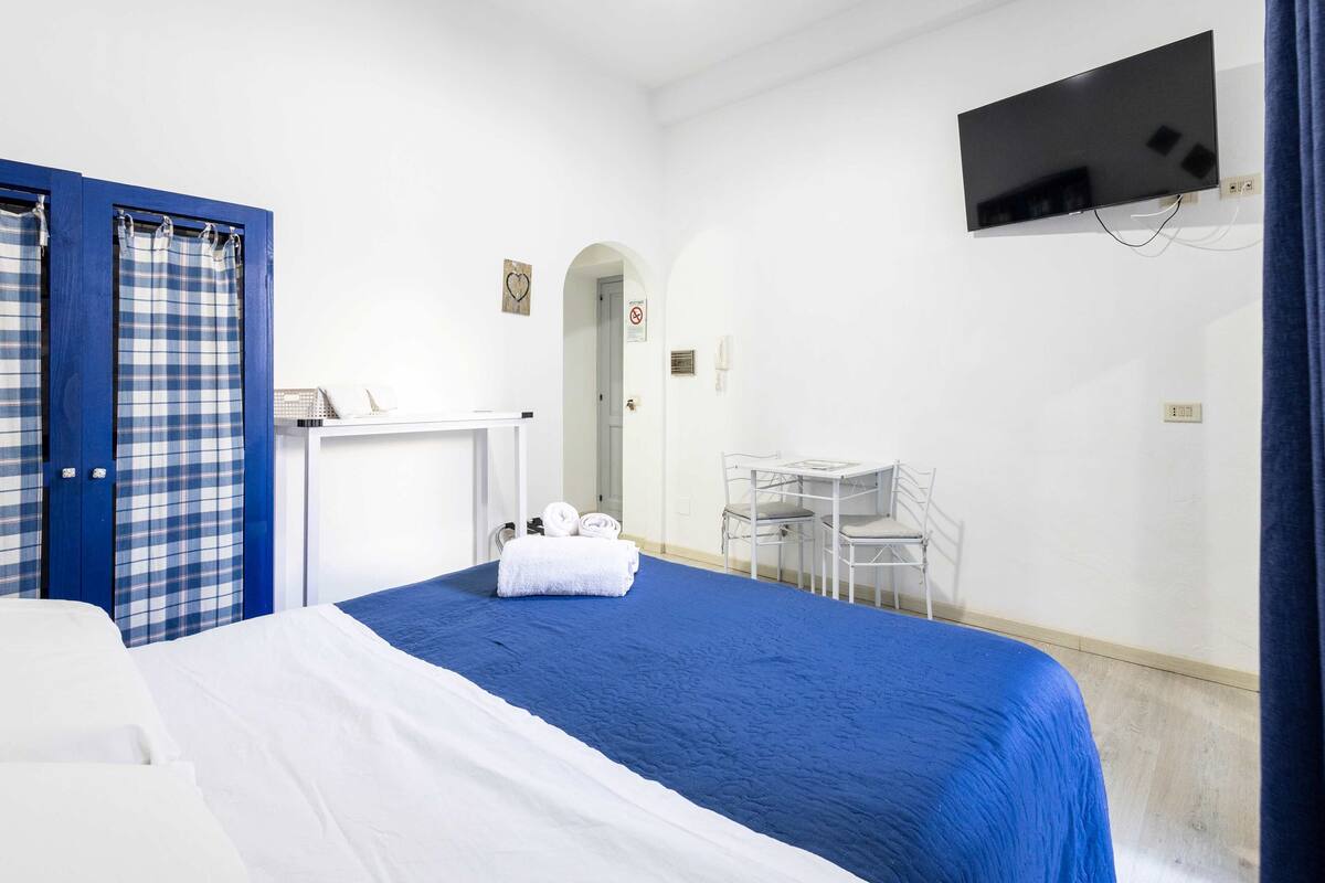 A hotel room with a bed, a desk, a chair, a TV, and a bathroom with a shower curtain.