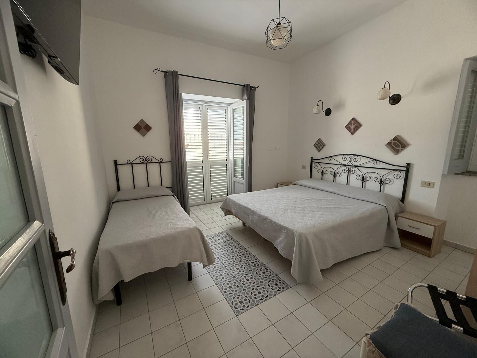 A bedroom with two beds, a window with curtains, a patterned rug, and a hanging light fixture.