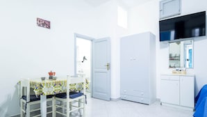 A small, bright room with a dining table, chairs, a wardrobe, and a mirror.