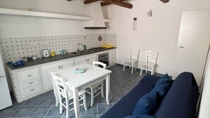 A compact kitchen with a dining area, featuring a white table and chairs, a blue sofa, and a tiled floor.