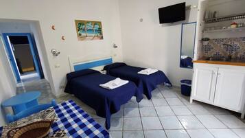 Quarto de hotel com duas camas, uma mesinha, televisão e cozinha.