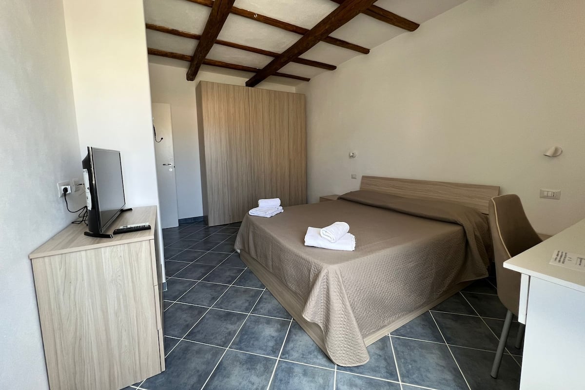 A hotel room with a bed, a desk, a television, and a wardrobe.