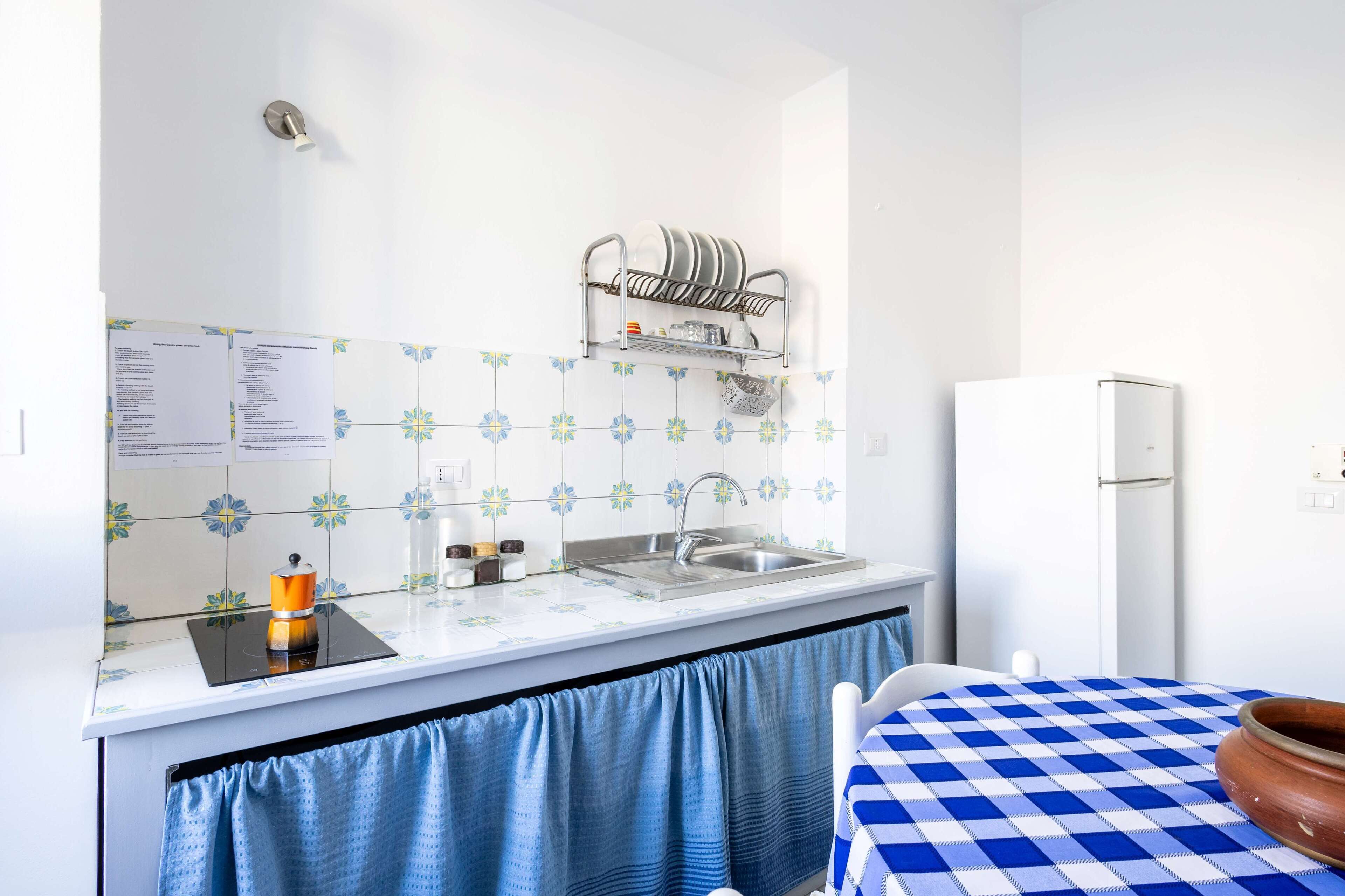 A kitchen with a sink, a dish rack, a stove, and a refrigerator.
