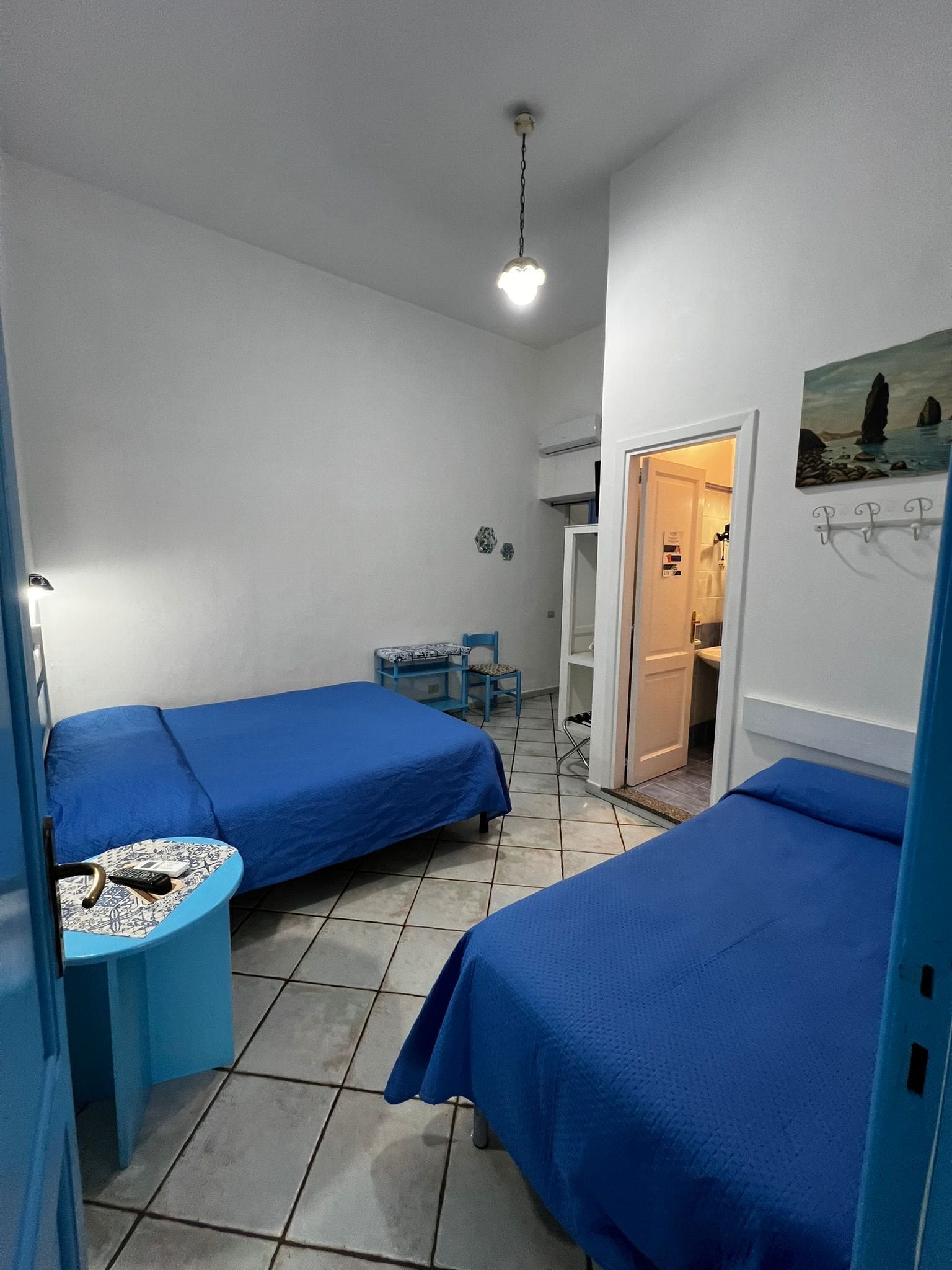 Een kleine, schone kamer met twee eenpersoonsbedden, een tafeltje met een stoel en een deur naar de badkamer.
