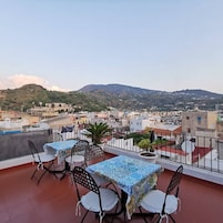 Una terraza con una mesa y sillas, una planta en maceta y vistas a una ciudad con montañas al fondo.