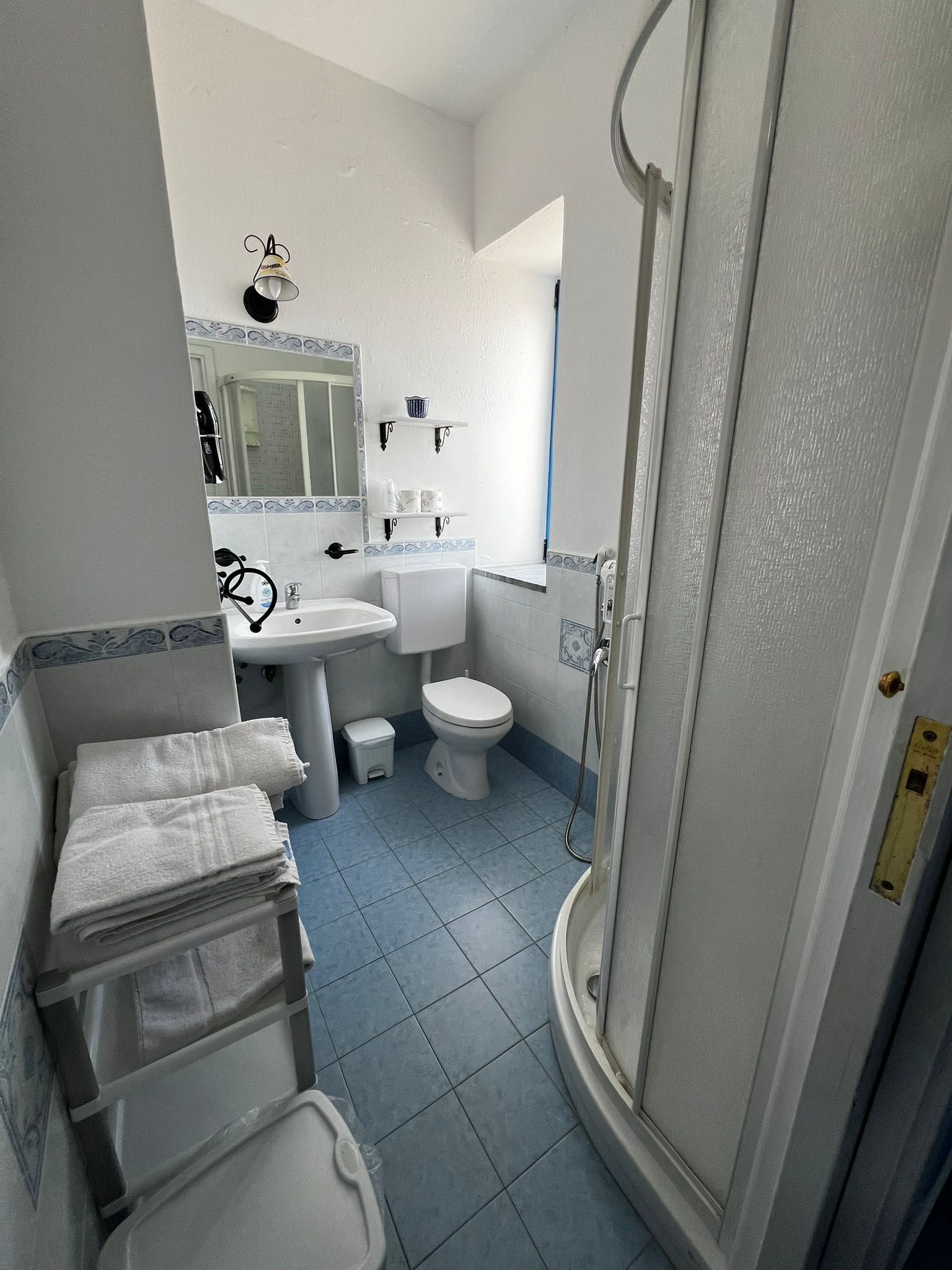 A bathroom with a sink, toilet, and shower. There are towels stacked on a shelf.