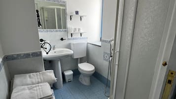 A bathroom with a sink, toilet, and shower. There are towels stacked on a shelf.