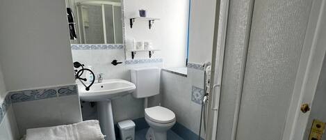 A bathroom with a sink, toilet, and shower. There are towels stacked on a shelf.