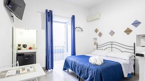 A hotel room with a bed, a desk, a TV, and a balcony with blue curtains.