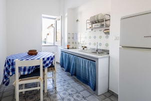 A compact kitchen with a window, a table with a checkered tablecloth, and a white refrigerator.