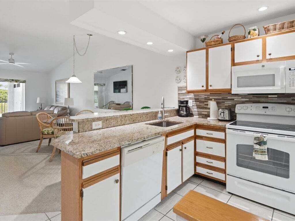 A modern kitchen with white cabinets, a microwave, an oven, and a sink. There is a dining area with a table and chairs.