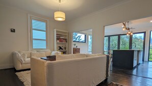 A modern living room with a white sofa, a bookshelf, and a kitchen area visible through an open door. - Your CBD Treetop Base | Parking, Wifi & Views (Launceston City)