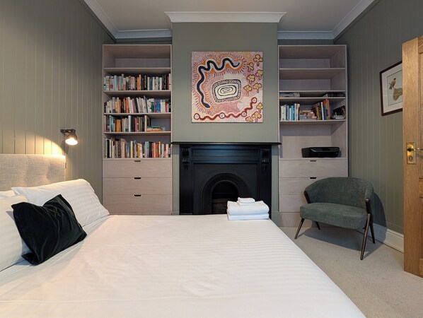 A bedroom with a large bed, a fireplace, bookshelves, and a chair.