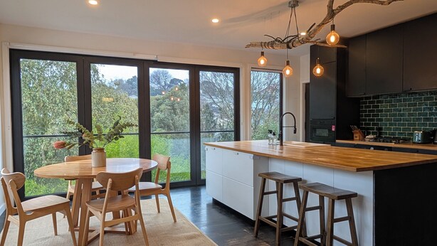 A modern kitchen with a large island, wooden chairs, and a view of greenery through large windows. - Your CBD Treetop Base | Parking, Wifi & Views (Launceston City)