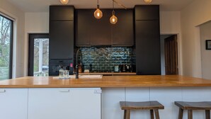 A modern kitchen with a wooden island, black cabinetry, and a backsplash of blue tiles. - Your CBD Treetop Base | Parking, Wifi & Views (Launceston City)